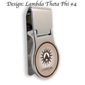 以下が含まれることがあります： スタイリッシュな太陽と三角形が描かれた、ブラウンとホワイトの丸いロゴがついたシルバーのマネークリップ。ロゴには「LAMBDAS EST. 1975」の文字が書かれています。