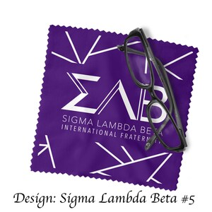 Może przedstawiać: Fioletowy ściereczka z mikrofibry do czyszczenia z białym logo Sigma Lambda Beta i tekstem "Sigma Lambda Beta International Fraternity". Na ściereczce leży para czarnych okular&oacute;w.