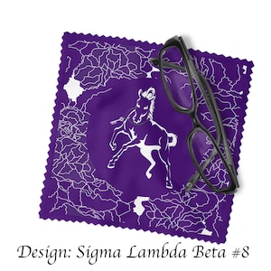 Könnte beinhalten: Ein violettes Mikrofaser-Reinigungstuch mit einem weißen Pferd und einem Schlüssel-Design. Das Tuch ist gefaltet und ein Paar schwarze Brillen liegt darauf. Der Text "Design: Sigma Lambda Beta #8" befindet sich am unteren Rand des Bildes.
