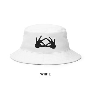 May include: White bucket hat with a black silhouette of two hands forming a triangle shape.
