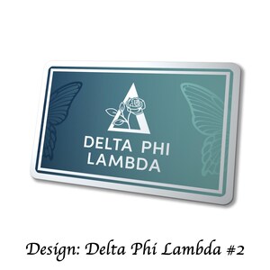 May include: A rectangular sticker with a white border and a gradient teal background. The sticker features a white triangle with a rose and the text "DELTA PHI LAMBDA". Butterfly wing outlines are on each side. The text "Design: Delta Phi Lambda #2" is below.