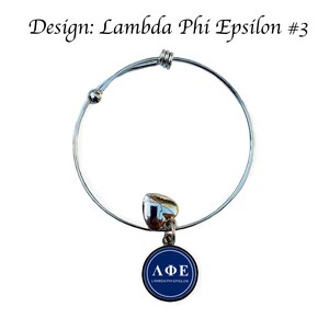 May include: A silver expandable bracelet with a blue charm that says "&Lambda;&Phi;&Epsilon; LAMBDA PHI EPSILON".