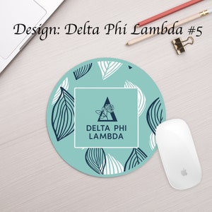 Może przedstawiać: Okrągła podkładka pod mysz w kolorze turkusowym z wzorem białych i czarnych liści. W środku znajduje się biały kwadrat z czarnym tr&oacute;jkątem i wzorem r&oacute;ży. Tekst "DELTA PHI LAMBDA" jest w czarnych literach wewnątrz kwadratu.
