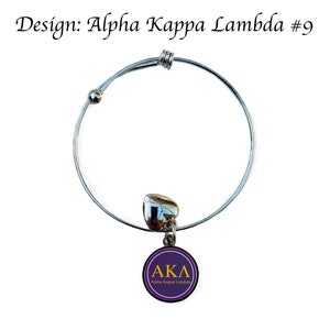 Puede incluir: Un brazalete extensible de plata con un dije en forma de coraz&oacute;n y un dije redondo con las letras "AKA" y el texto "Alpha Kappa Lambda" en letras doradas sobre un fondo morado.