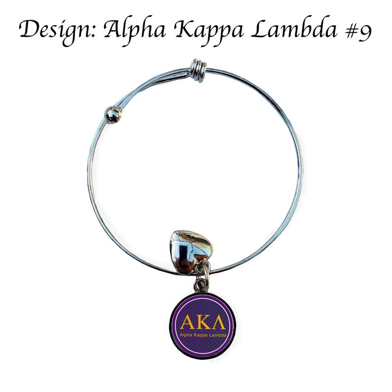 Puede incluir: Un brazalete extensible de plata con un dije en forma de coraz&oacute;n y un dije redondo con las letras "AKA" y el texto "Alpha Kappa Lambda" en letras doradas sobre un fondo morado.