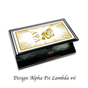 Peut inclure: Un porte-cartes de visite argent&eacute; avec un fond blanc et des lettres dor&eacute;es. Les lettres disent "AYA" et pr&eacute;sentent une rose dor&eacute;e.