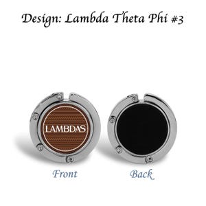 Może przedstawiać: Srebrny haczyk do torebki z okrągłym, brązowo-białym wzorem z przodu z napisem "LAMBDAS" i geometrycznym wzorem. Tył jest czarny. U góry znajduje się napis "Design: Lambda Theta Phi #3".