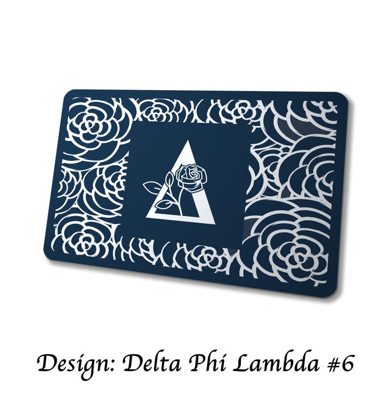 May include: A navy blue rectangular item with a white floral cut-out border. The center features a white triangle with a rose and the Greek letter delta. The text "Design: Delta Phi Lambda #6" is at the bottom.