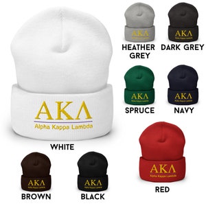 Op de afbeelding: Een verzameling gebreide mutsen in verschillende kleuren, waaronder wit, zwart, bruin, rood, donkergrijs, grijs, marineblauw en spar. Elke muts heeft de Griekse letters "AKA" in gouden borduurwerk en de woorden "Alpha Kappa Lambda" in kleiner gouden borduurwerk.