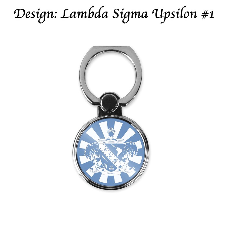 May include: A silver phone ring holder with a round, blue and white emblem. The emblem features a crest design with palm trees and the text "Design: Lambda Sigma Upsilon #1". The ring is attached to a swivel base.