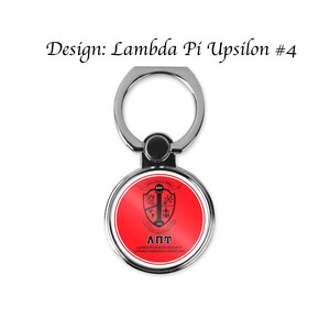 Op de afbeelding: Een zilveren telefoonringhouder met een rode cirkel met een zwart-wit wapenschild met de tekst "&Lambda;&Pi;&Upsilon; LAMBDA PI UPSILON SORORITY LATINAS PODEROSAS UNIDAS INC"