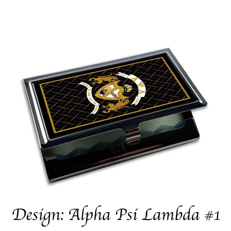 Peut inclure: Un porte-cartes de visite noir et or avec un blason de fraternit&eacute; grecque repr&eacute;sentant un bouclier, des lions et les lettres "Alpha Psi Lambda".