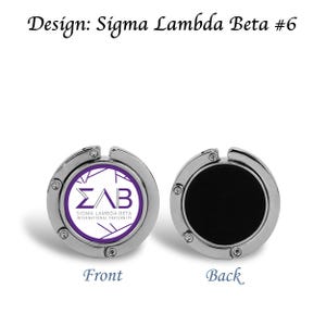 May include: Two silver-colored purse hangers. One displays the Sigma Lambda Beta International Fraternity logo in purple and white. The other has a black surface. Text on the image reads "Design: Sigma Lambda Beta #6", "Front", and "Back".