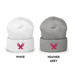 以下が含まれることがあります： 白とヘザーグレーのニットビーニー2つ。ピンクの刺繍で、2つの手が「OK」サインを作り、Xの形になっている。