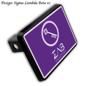 May include: Black trailer hitch cover with a purple background featuring a white key inside a white circle. The text "ΣAB" and "SIGMA LAMBDA BETA INTERNATIONAL FRATERNITY" are also displayed in white. The design is labeled "Design: Sigma Lambda Beta #1".