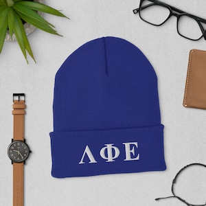 May include: A royal blue beanie with a white embroidered Greek letter design that reads "ΛΦΕ".