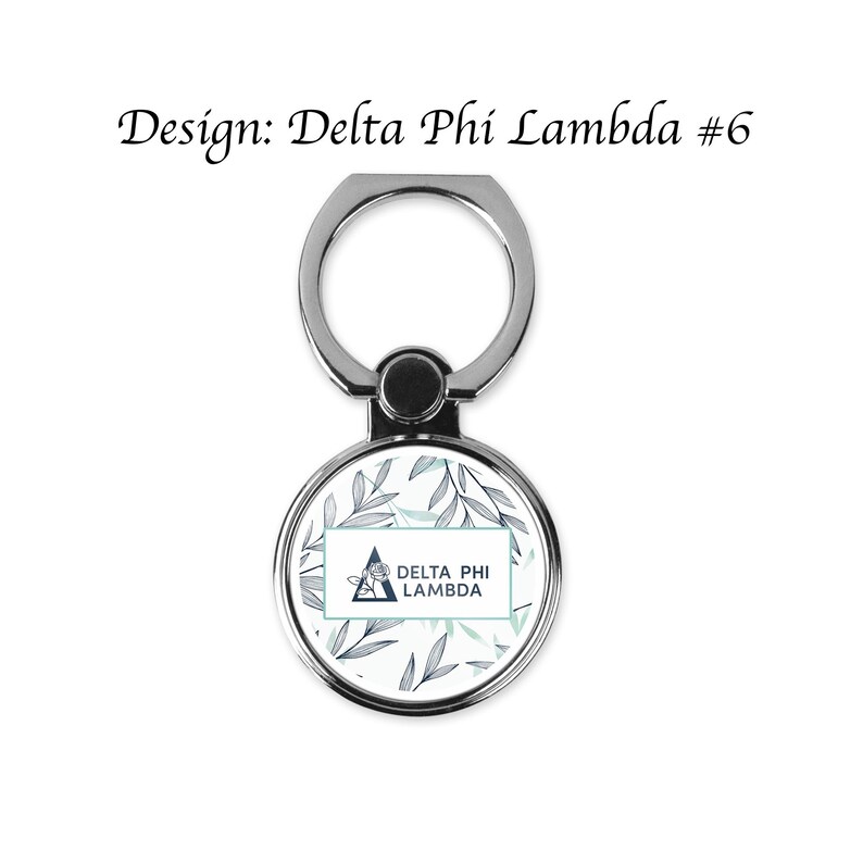 Op de afbeelding: Een zilveren telefoonringhouder met een ronde, patroonvormige voorkant. De voorkant heeft een bloemenontwerp in blauw- en groentinten, met de tekst "DELTA PHI LAMBDA" in een rechthoekig kader. De tekst "Design: Delta Phi Lambda #6" staat boven de ring.