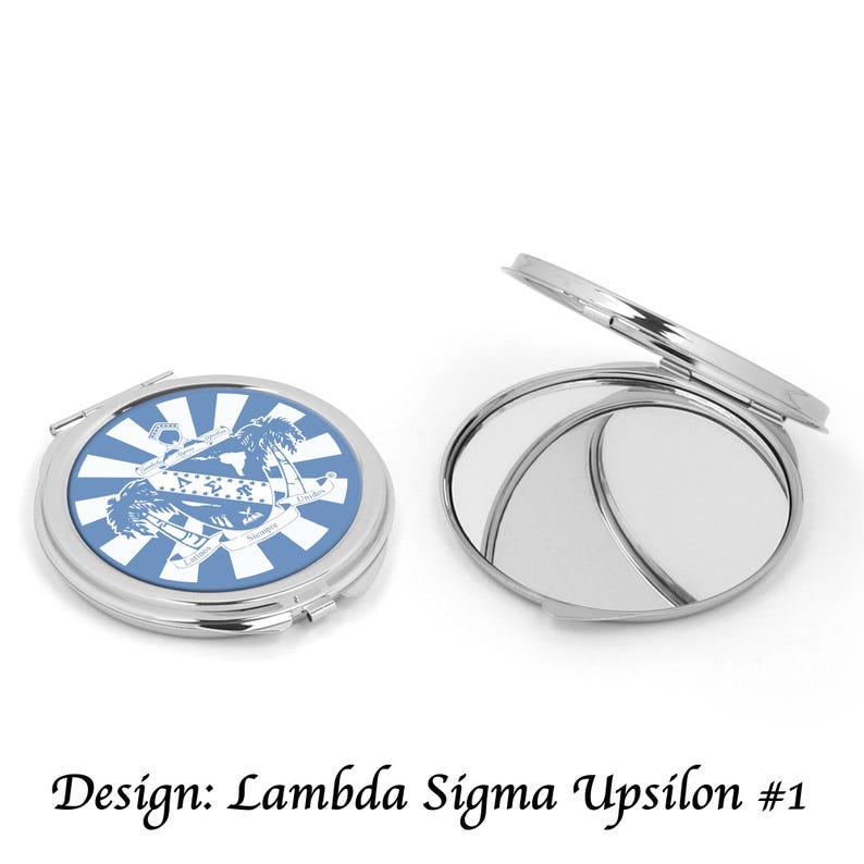 May include: Two silver compact mirrors. One is closed, displaying a blue and white design with text and a crest. The other is open, revealing two reflective surfaces. The text at the bottom reads "Design: Lambda Sigma Upsilon #1".