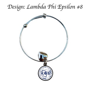 May include: A silver expandable bracelet with a charm featuring a white circle with a blue Lambda Phi Epsilon logo and black lines.