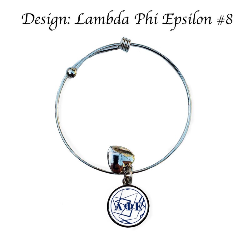 May include: A silver expandable bracelet with a charm featuring a white circle with a blue Lambda Phi Epsilon logo and black lines.