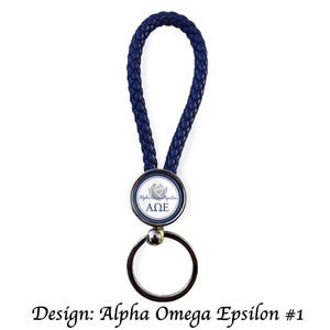 May include: A navy blue braided leather keychain with a silver-toned metal key ring. The keychain features a round emblem with the text "Alpha Omega Epsilon" and a rose design. The design is labeled "Design: Alpha Omega Epsilon #1".