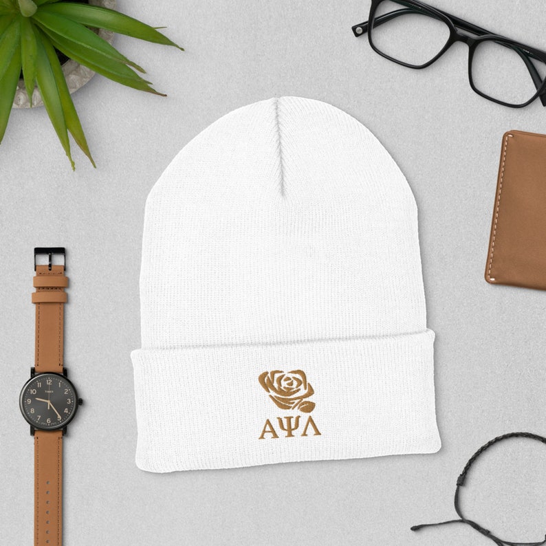 Op de afbeelding: Witte gebreide beanie met een bruine geborduurde roos en de letters "A&Phi;&Lambda;".