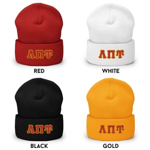 K&ouml;nnte beinhalten: Vier Beanies in verschiedenen Farben: Rot, Wei&szlig;, Schwarz und Gold. Jeder Hut tr&auml;gt die Buchstaben "&Lambda;&Pi;&Pi;&Gamma;" in einer kontrastierenden Farbe.