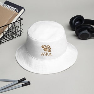 Könnte beinhalten: Weißer Bucket Hat mit einer braunen Rose und den Buchstaben "ΑΦΛ" auf der Vorderseite gestickt.