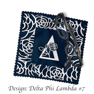 May include: A navy blue microfiber cleaning cloth with a white rose and triangle design. The cloth has a white border with a floral pattern. A pair of black eyeglasses is on top of the cloth.