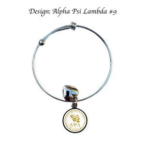 May include: A silver expandable bracelet with a charm featuring a white circle with a gold rose and the letters "&Alpha;&Psi;&Lambda;" in gold.
