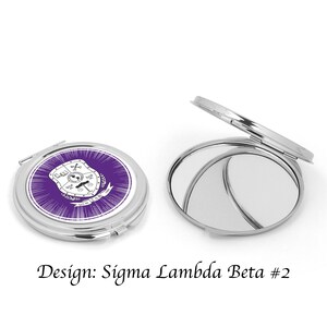Pu&ograve; includere: Uno specchio compatto argentato con un design viola e bianco che presenta uno scudo con una croce, una bilancia e un globo. Il testo "Sigma Lambda Beta" &egrave; sullo scudo. Lo specchio &egrave; chiuso.