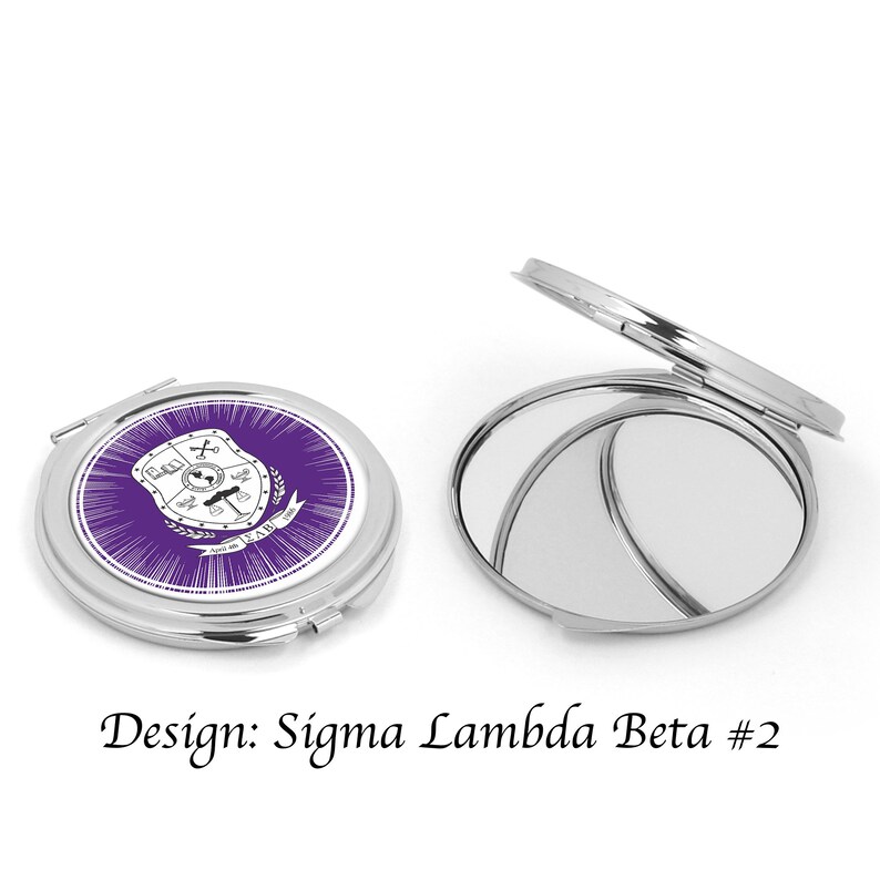 Pu&ograve; includere: Uno specchio compatto argentato con un design viola e bianco che presenta uno scudo con una croce, una bilancia e un globo. Il testo "Sigma Lambda Beta" &egrave; sullo scudo. Lo specchio &egrave; chiuso.