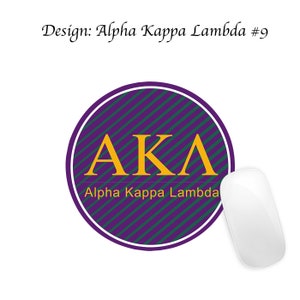 Pode incluir: Um tapete de rato circular com riscas roxas e verdes com as letras AKA em dourado e o texto "Alpha Kappa Lambda" em dourado.