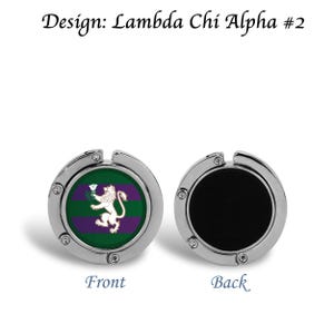 以下が含まれることがあります： 白いライオンと「Design: Lambda Chi Alpha #2」の文字が入った、緑と紫のエンブレムが付いたシルバーカラーのバッグフック。フックの裏側は黒色です。フックの前面には「Front」、背面には「Back」と表示されています。