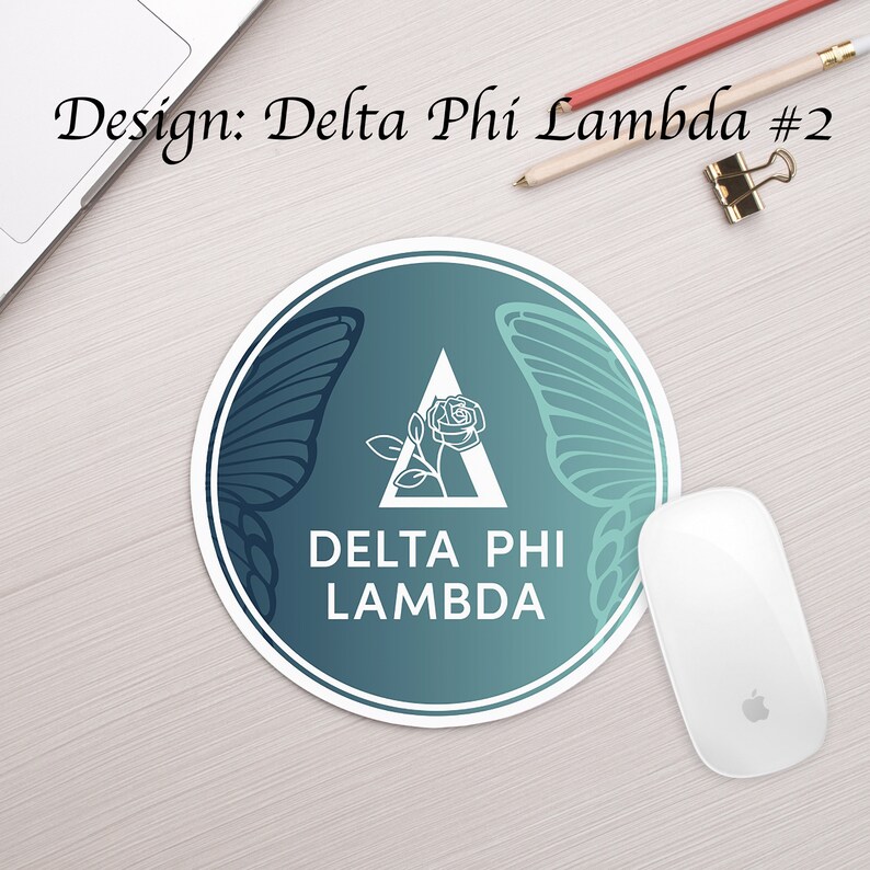 Może przedstawiać: Okrągła podkładka pod mysz w kolorze turkusowym i niebieskim z białym obramowaniem. W środku znajduje się biały tr&oacute;jkąt z r&oacute;żą w środku i tekstem "DELTA PHI LAMBDA". Po obu stronach tr&oacute;jkąta znajdują się dwa białe skrzydła motyla.