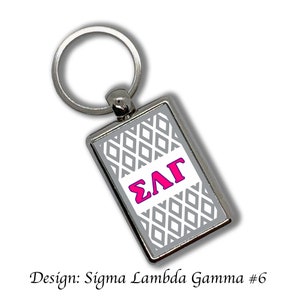 Puede incluir: Llavero rectangular plateado con un diseño geométrico gris y blanco. El centro presenta las letras griegas ΣΛΓ en rosa brillante. El texto "Design: Sigma Lambda Gamma #6" está en la parte inferior.