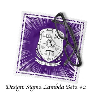 Może przedstawiać: Kwadratowy materiał w kolorze fioletowym i białym z czarno-białym herbem w środku. Herb przedstawia glob, wagę, klucz, książkę i lampę. Na materiale widoczny jest tekst "April 4th", "&Sigma;&Lambda;&Beta;" i "1986". Na materiale leżą czarne okulary.