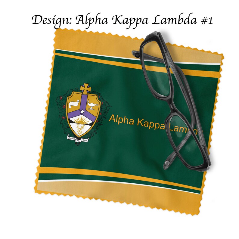 K&ouml;nnte beinhalten: Ein gr&uuml;nes und goldenes Mikrofaser-Reinigungstuch mit dem Wappen von Alpha Kappa Lambda und dem aufgedruckten Text "Alpha Kappa Lambda". Ein Paar schwarze Brillen liegt auf dem Tuch.