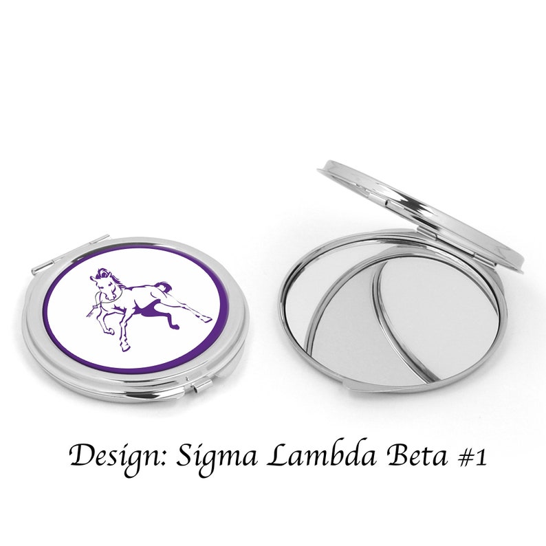 Pu&ograve; includere: Uno specchio compatto argentato con sfondo bianco e un design a cavallo viola. Lo specchio &egrave; chiuso e il design &egrave; visibile sul davanti. Il testo "Design: Sigma Lambda Beta #1" &egrave; sotto lo specchio.