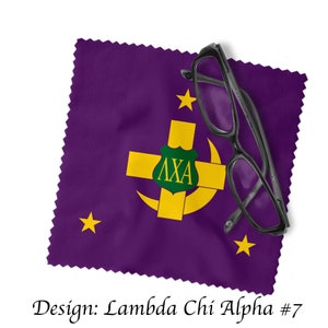 May include: Purple microfiber cleaning cloth with a gold crescent moon, cross, and shield with the letters "ΛΧΑ" in green. The cloth is folded and a pair of black eyeglasses are on top of it.