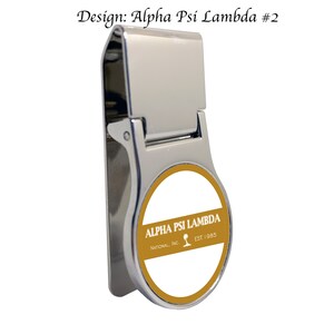 May include: A silver money clip with a round, gold-colored emblem featuring the text "ALPHA PSI LAMBDA", "NATIONAL, INC.", and "EST. 1985".