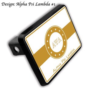 Op de afbeelding: Zwarte trekhaakafdekking met een wit en goud ontwerp. Het ontwerp bevat een gouden streep, een cirkelvormig embleem met de Griekse letters AΨΛ en de tekst "ALPHA PSI LAMBDA". De tekst "Design: Alpha Psi Lambda #1" is ook zichtbaar.