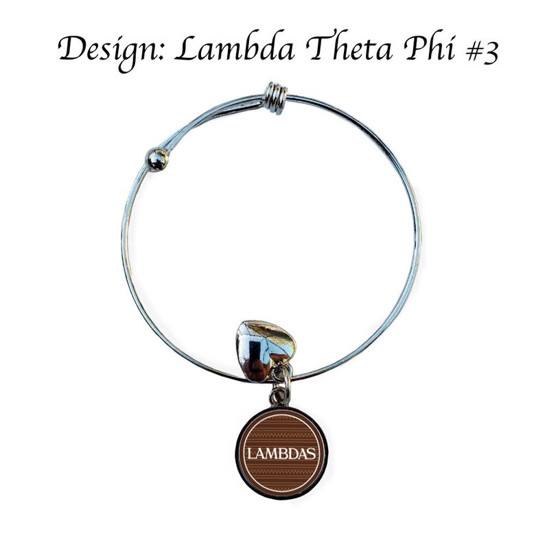 Op de afbeelding: Een zilveren uittrekbaar armband met een bruine bedel met de tekst "LAMBDAS" in wit. De bedel heeft een gepatroneerd ontwerp.