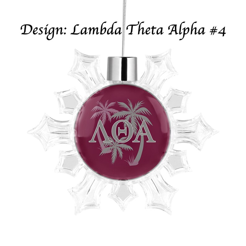 K&ouml;nnte beinhalten: Ein klarer Schneeflocken-Weihnachtsschmuck mit einem weinroten Mittelteil. Der Mittelteil zeigt Palmen und die griechischen Buchstaben &Lambda;&Theta;A in Silber. Der Text "Design: Lambda Theta Alpha #4" befindet sich dar&uuml;ber.