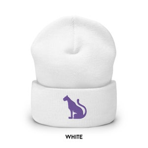 以下が含まれることがあります： 紫色の刺繍で座っているパンサーのシルエットが施された白いビーニー