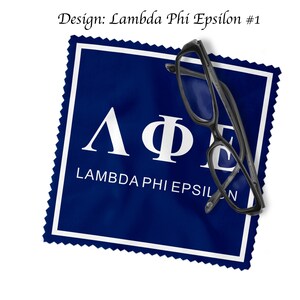 May include: A navy blue microfiber cleaning cloth with a white border and the Greek letters Lambda, Phi, and Epsilon. The text "LAMBDA PHI EPSILON" is below the letters. Black eyeglasses rest on the cloth.