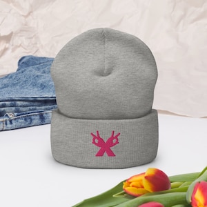 Op de afbeelding: Grijze beanie met een roze geborduurd ontwerp van twee handen die het vredesteken maken. De handen zijn gekruist bij de polsen, waardoor een 'X' vormt.