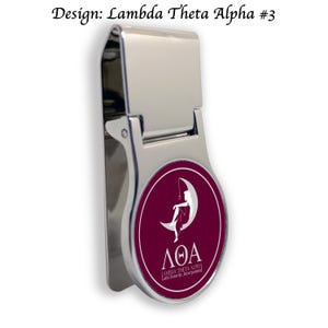 Può includere: Un fermaglio per soldi in argento con un design rotondo di colore granata che presenta una silhouette bianca di una donna seduta su una luna crescente. Il design include anche il testo "ΛΘΑ LAMBDA THETA ALPHA Latin Sorority, Incorporated".