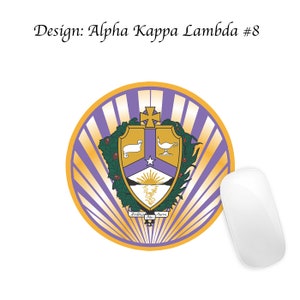 Pode incluir: Um tapete de rato redondo de cor roxa e dourada com um bras&atilde;o que apresenta um cordeiro branco, uma l&acirc;mpada dourada e uma estrela. O bras&atilde;o &eacute; rodeado por uma coroa de louro verde e o texto "Audentes Fortuna Juvat".