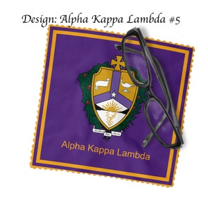 K&ouml;nnte beinhalten: Lilafarbener und goldener Stoffquadrat mit einem Wappen, das einen wei&szlig;en Stern, einen Sonnenaufgang, ein Lamm und eine Lampe zeigt. Der Text "Alpha Kappa Lambda" ist unter dem Wappen gedruckt.